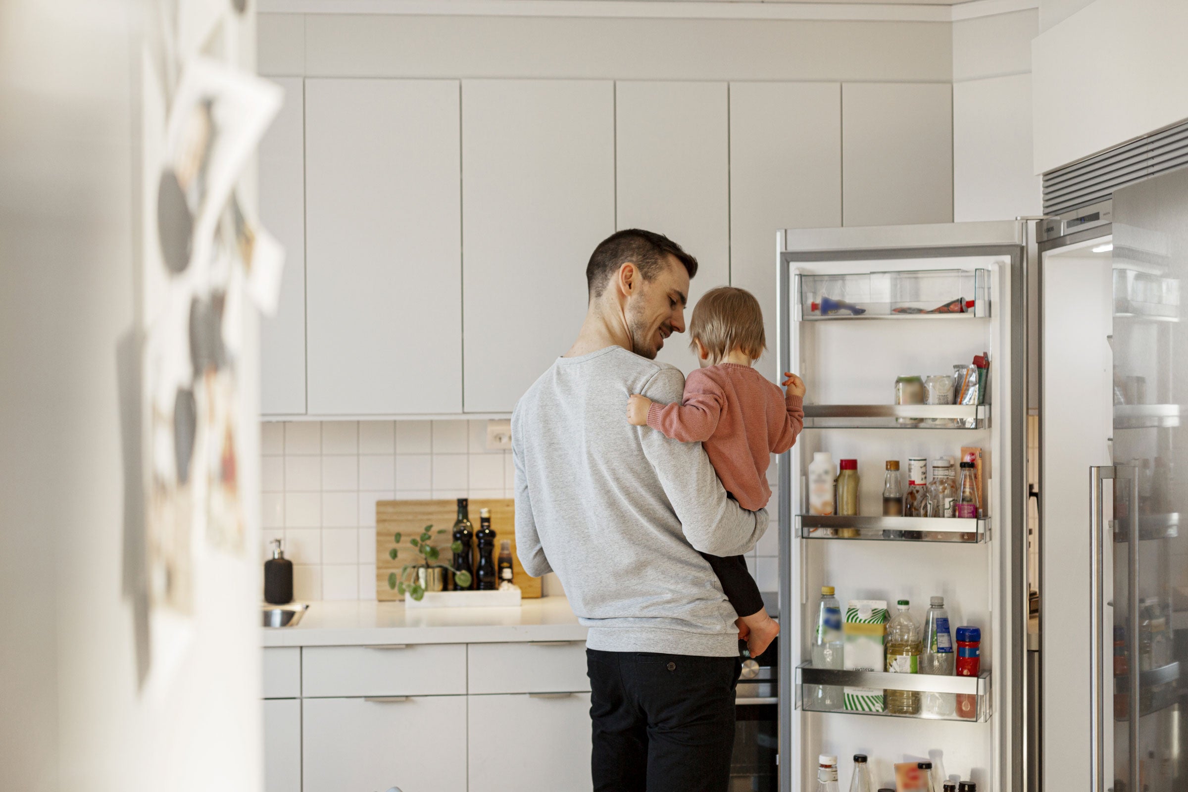 Father holding a child and opening a refrigerator door