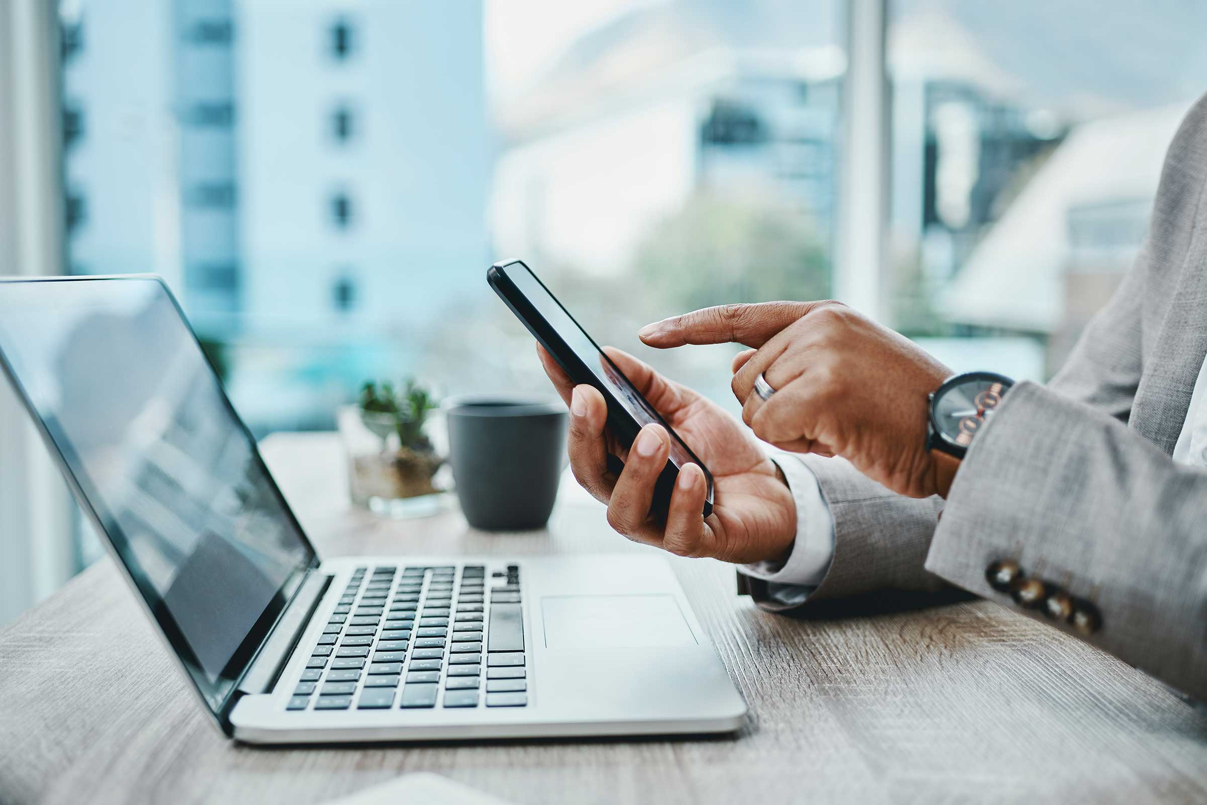 Business professional using a smartphone and laptop in a modern office
