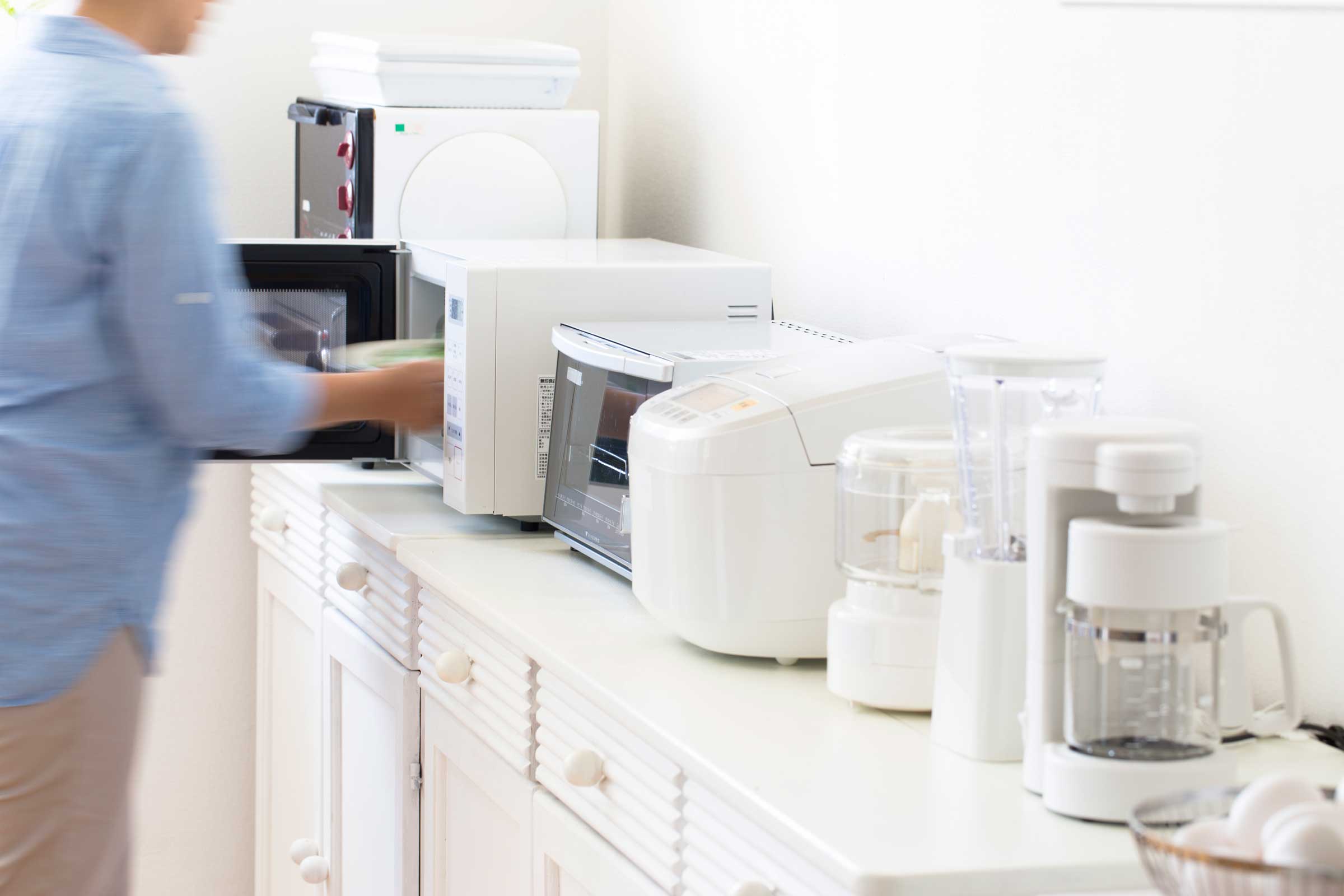 Person using a microwave sitting on a white countertop filled with white kitchen appliances
