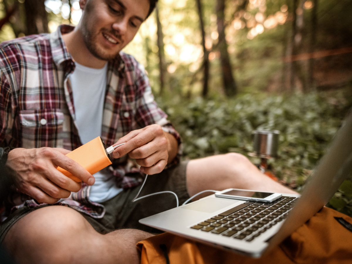 A person working from a camp inside the forest, connecting a power bank to a laptop