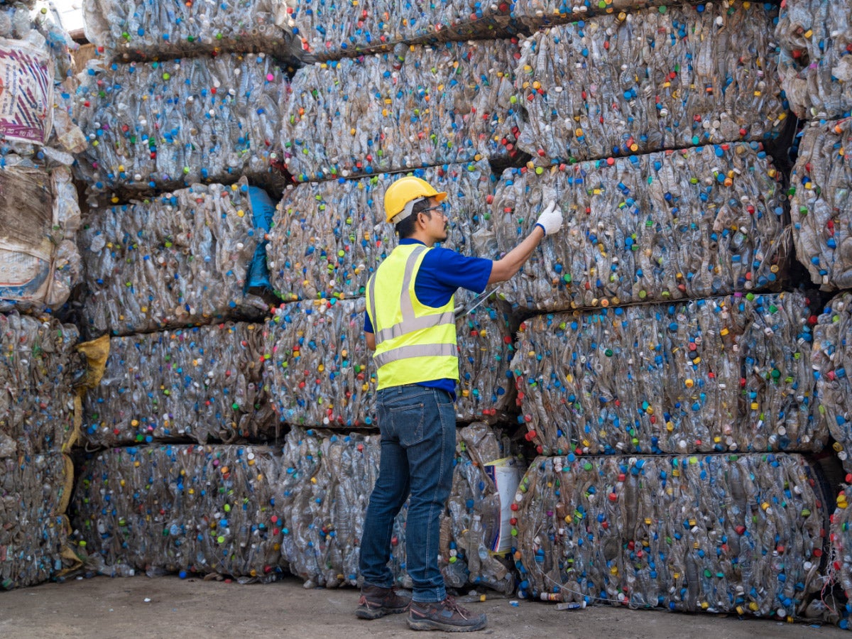 Worker inspects stacks of bales of recycled plastic